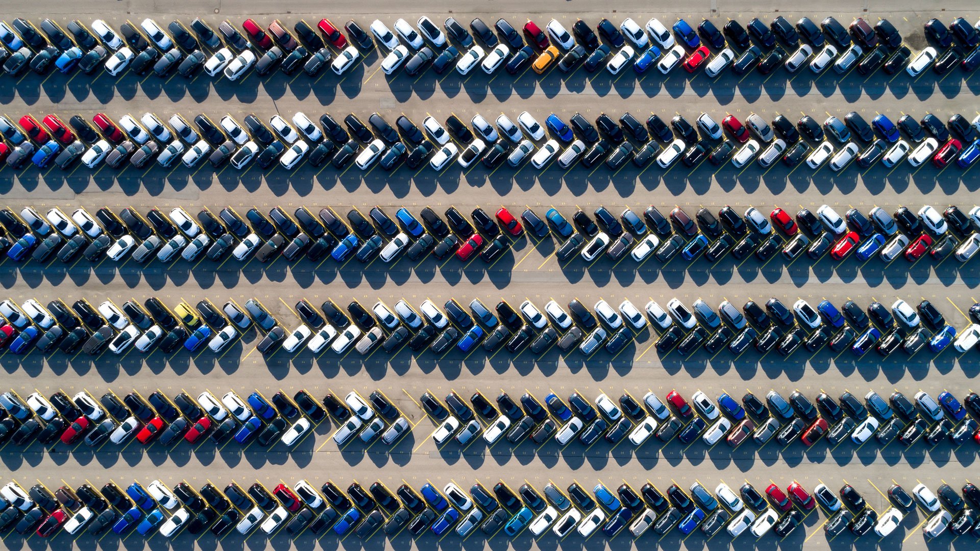 Aerial view of a bright dealer lot filled with rows of cars for sale
